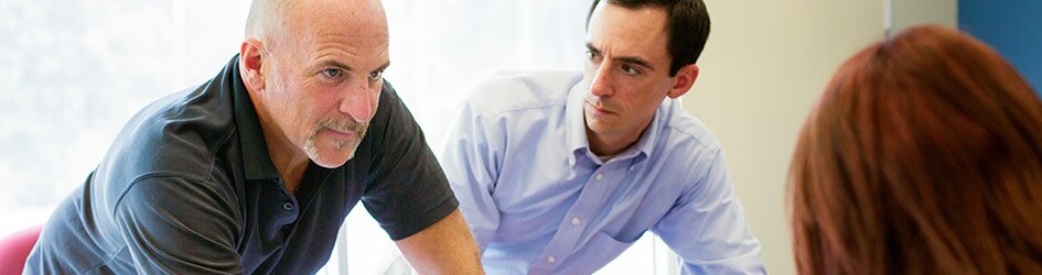 An older man looks aggressively at a colleague across a conference table