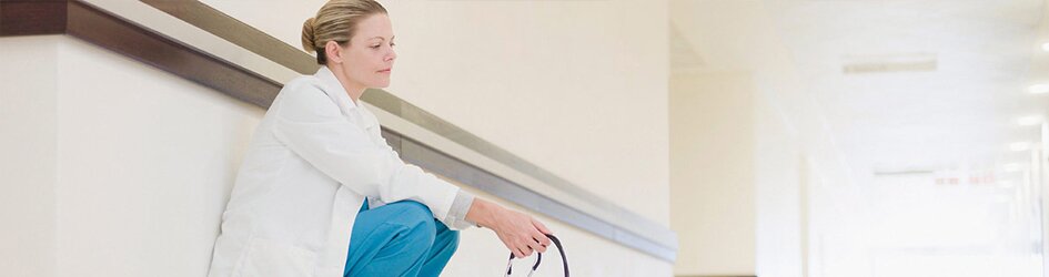 A troubled female doctor crouches in the hallway