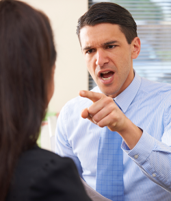 An older businessman threatens a female subordinate across a conference table